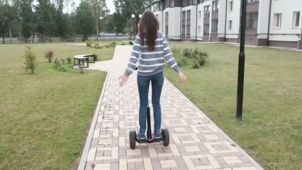 Brunette femme roule sur scooter gyroscope près de la maison, vue arrière . — Video