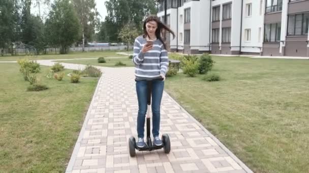Vacker brunett kvinna är rullande på gyro scooter nära hem och titta på mobiltelefon. — Stockvideo