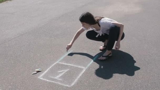 Mulher desenha um hopscotch no asfalto com giz colorido . — Vídeo de Stock