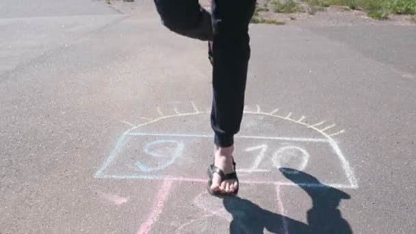 Ragazza adolescente salta giocando hopscotch in strada. Gambe da primo piano. Vista frontale . — Video Stock