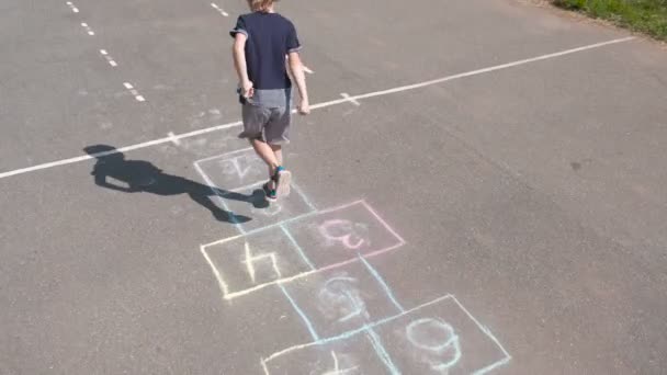 Chico salta jugando a la hopscotch en la calle. Vista trasera . — Vídeos de Stock