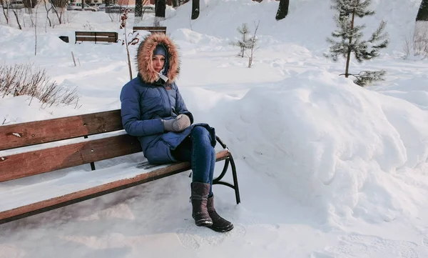 Woman is sitting on bench in winter city park in sunny day.