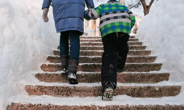 Крупным планом мама и сыновья поднимаются по заснеженной лестнице, лестнице. Зимний городской парк в снежный день с падающим снегом . — стоковое фото