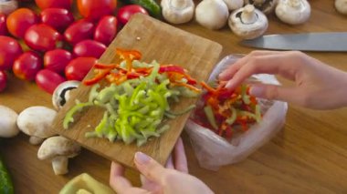 Kesme koymak WOMANS yakışıklı kırmızı ve yeşil biber bir plastik paket mutfak masasında dondurma için