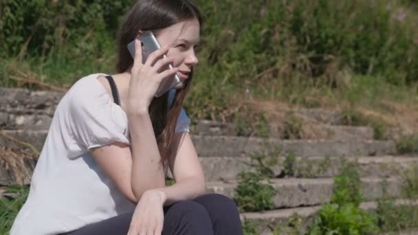 Mujer joven hablando de teléfono móvil sentado en el parque . — Vídeos de Stock