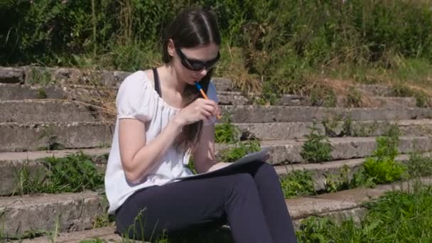 Chica joven haciendo sus tareas y deberes sentado en el parque. Estudiante universitario . — Vídeos de Stock