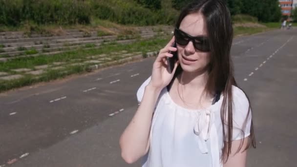Νεαρή γυναίκα μιλάμε κινητό τηλέφωνο περπάτημα στο γήπεδο. — Αρχείο Βίντεο