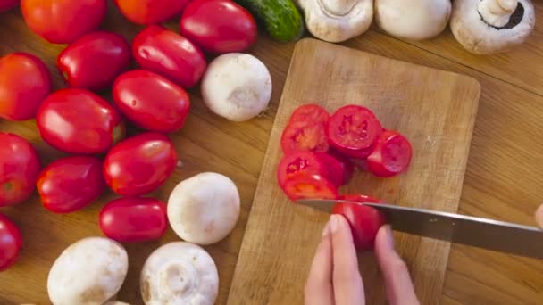 Frauenhände schneiden Tomaten auf dem Holzsteg auf dem Küchentisch. Ansicht von oben. — Stockvideo