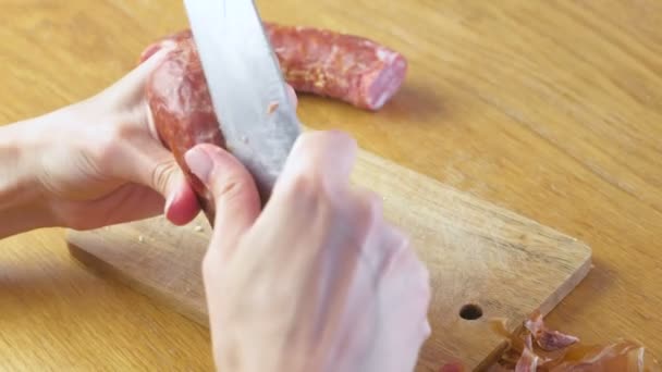 Le mani delle donne stanno sbucciando la salsiccia affumicata dalla buccia . — Video Stock