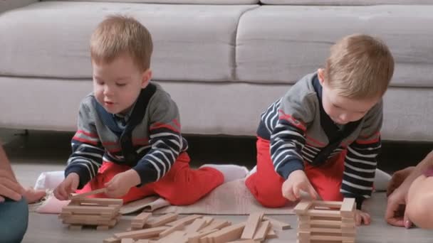 Famille maman, papa et deux frères jumeaux jouent ensemble construire à partir de blocs de bois sur le sol . — Video