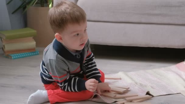 Boy construit une tour à partir de blocs de bois assis sur le sol près du canapé . — Video