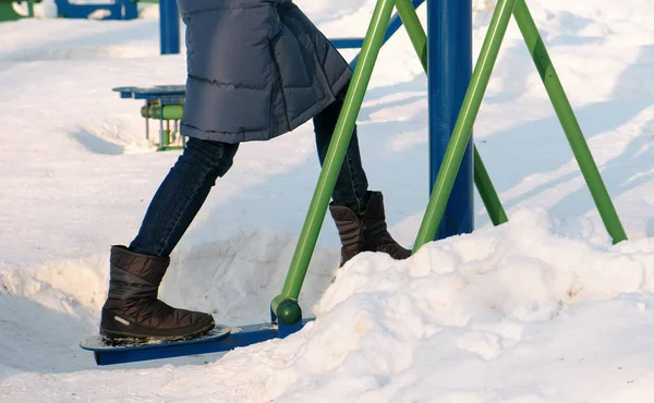 As pernas de mulher de close-up envolvem-se no simulador de esqui no Parque de inverno na cidade. Neve deriva ao redor . — Fotografia de Stock