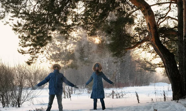 Homem e uma mulher de jaquetas azuis jogam neve na floresta de inverno e sorriem. Vista frontal — Fotografia de Stock