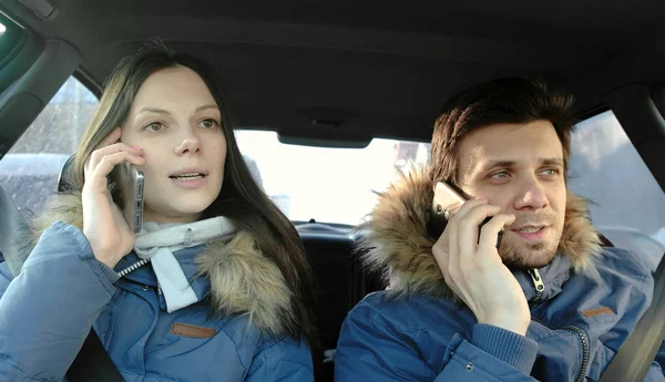 Homme et femme parlant leurs téléphones portables et souriant assis dans la voiture. Vue de face . — Photo