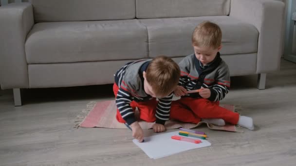 Twee tweeling broers peuters trekken samen markeringen zittend op de vloer. — Stockvideo