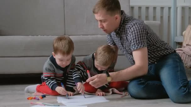 Familie vader en twee tweelingbroers trekken samen markeringen en voelde pennen zittend op de vloer. — Stockvideo