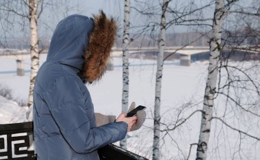 Mavi ceket kürk başlık ile aşağı tanınmaz halde kadın cep telefonunu kış Park içinde ileti yazıyor
