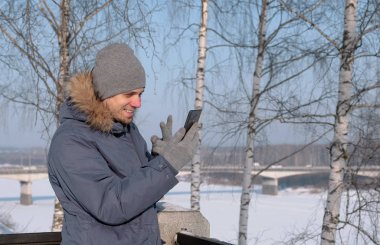 Video sohbet ve kış parkta gülümseyen için cep telefonu kullanarak kürk başlık ceketle aşağı mavili adam.