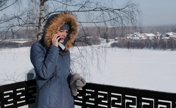 Женщина в синем пиджаке с меховым капюшоном звонит на мобильный в зимнем парке . — стоковое фото