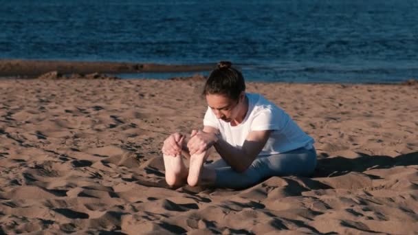 Woman doing yoga on the beach by the river in the city. Beautiful view in Paschimottanasana, Sirsasana pose. — Stock Video