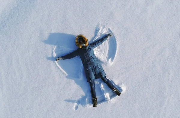 Woman makes snow angel laying in the snow. Top view. Aerial foto.