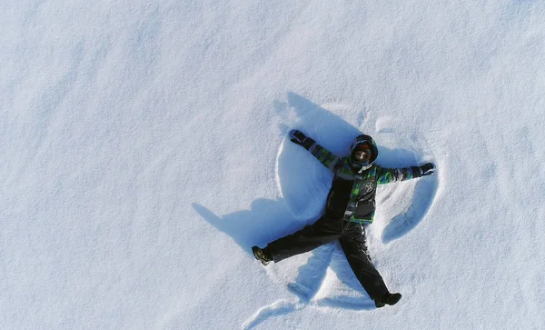 Menino de 7 anos faz anjo da neve na área de neve. Fotografia aérea . — Fotografia de Stock