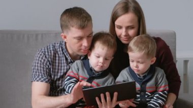 Aile tablet ile. Anne, baba ve iki oğlu ikizler tablet kanepe oturma bakarak.