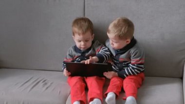 İki ikiz kardeşler birbirlerinin kanepede oturan tablet götürün. Çocuklar tablet üzerinde oyun.