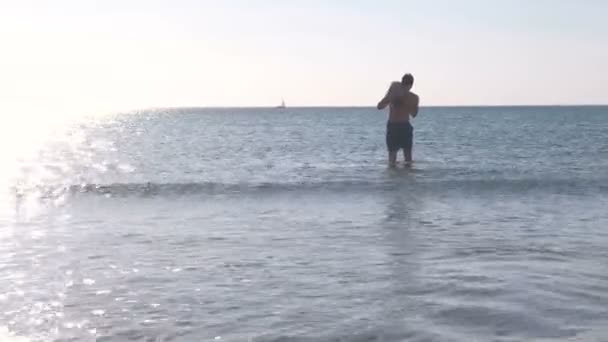 O pai e o filho estão a brincar juntos na água do mar ao pôr-do-sol. Natação no mar . — Vídeo de Stock