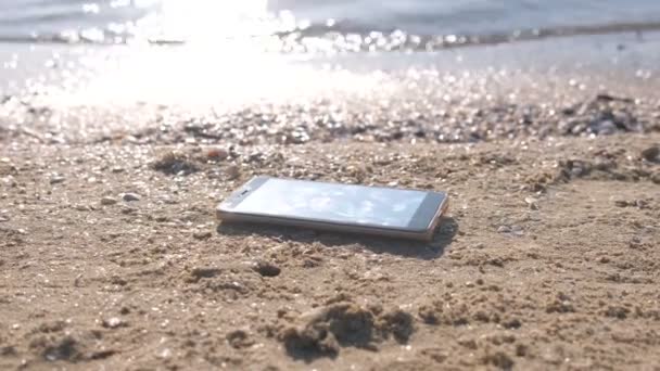 Teléfono móvil en la playa de arena con olas . — Vídeos de Stock