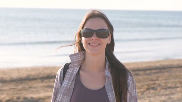 Jovem feliz sorrindo mulher morena em óculos de sol na praia de areia junto ao mar . — Vídeo de Stock