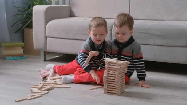 Zwillinge Jungen Brüder bauen einen Turm aus Holzklötzen sitzt auf dem Boden neben dem Sofa in ihrem Zimmer. — Stockvideo