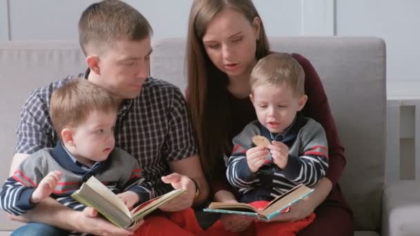 家族のお母さん、お父さんと 2 つの双子の兄弟は、ソファに座って本を読みます。家族の読書の時間. — ストック動画