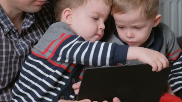 Familie met tablet. Moeder, vader en twee zonen twins spelen op tablet zitten in de Bank. — Stockvideo