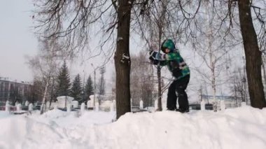 Düşen kar karlı gün içinde bir ağaç dalı kış city Park üzerinde sallanan çocuk.