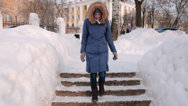 Kvinnan går ner på en snöig stege, trappa. Vinterparken i staden under dagen i snöiga väder med fallande snö. — Stockvideo