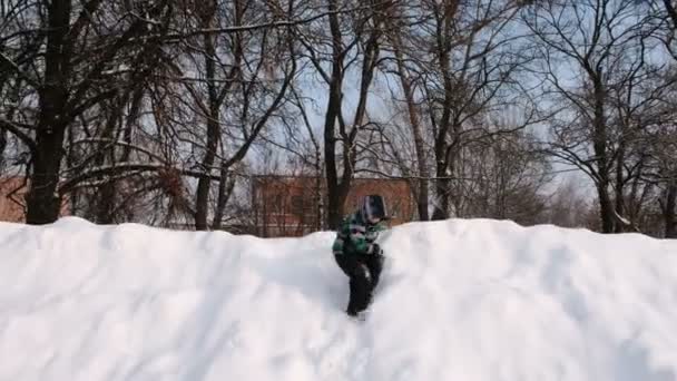 O rapaz joga na neve. Menino corre e desce de uma alta neve deriva . — Vídeo de Stock