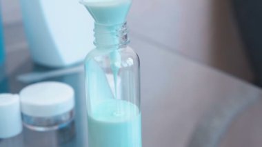 Büyük bir huni küçük bir şişe mavi şampuan dökün. Kavanoz dizi seyahat. Şişe yakın çekim.