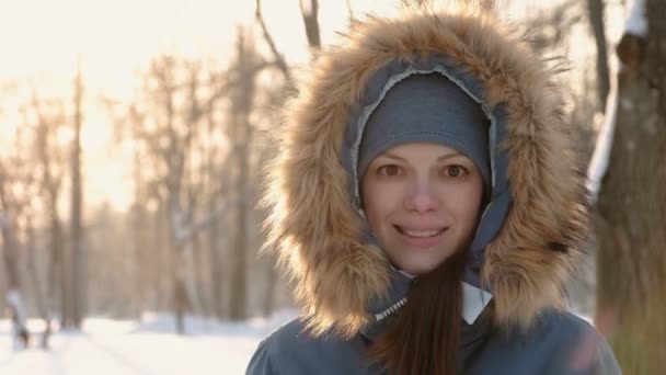 Close-up cara de mulher em capuz de pele olhando para a câmera e sorrindo no parque ensolarado inverno. Direita em vídeo — Vídeo de Stock