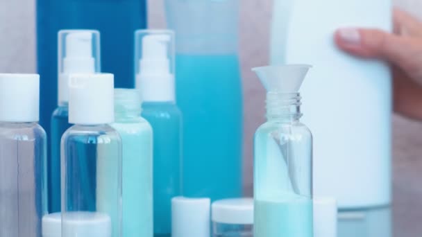 Le mani delle donne versano lo shampoo blu in una piccola bottiglia di grande attraverso un imbuto. Set di barattoli da viaggio. Primo piano della bottiglia . — Video Stock