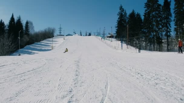 L'uomo in giacca gialla scende dalla montagna su un pendio di snowboard vicino all'impianto di risalita . — Video Stock