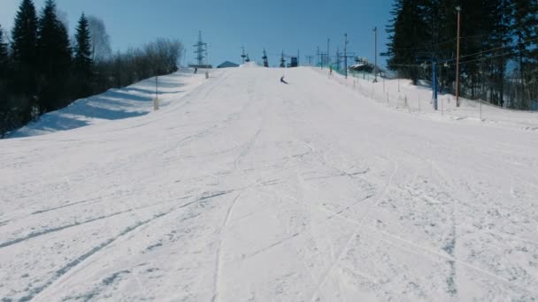 Tonårig pojke 12 år i blå kostym glidande på en snowboard från snö nedstigningen nästa sky lift. Visa från fjärran. — Stockvideo