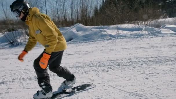 Closeup man in yellow jacket sliding on a snowboard in city park. — Stock Video