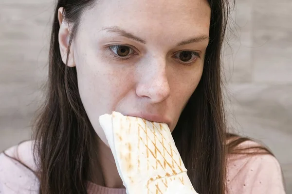 Giovane donna bruna che mangia danaro o Shawarma seduta in un caffè . — Foto Stock