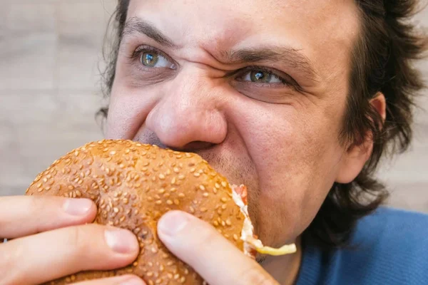 Портрет молодого человека, поедающего гамбургер в кафе . — стоковое фото