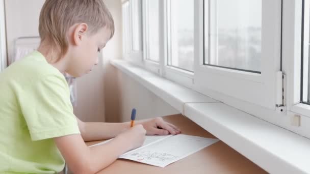 Menino da escola aprende a escrever cartas sentadas à mesa. Fazer trabalhos de casa . — Vídeo de Stock