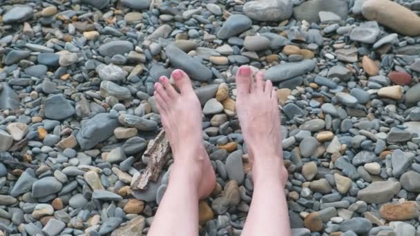 Womens voeten tegen de zee in stenen strand. — Stockvideo