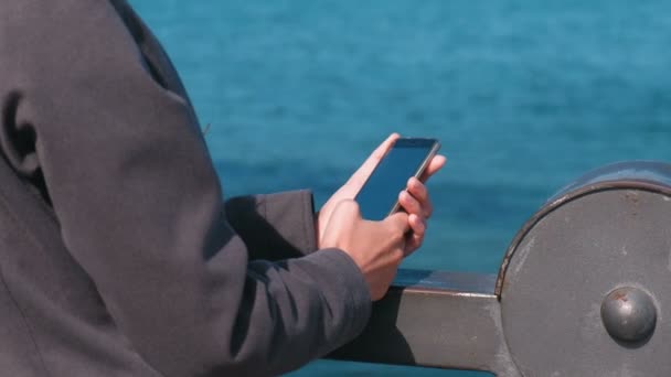 Dames handen Typ een bericht op een mobiele telefoon die op het water door de zee op een Sunny herfstdag. — Stockvideo