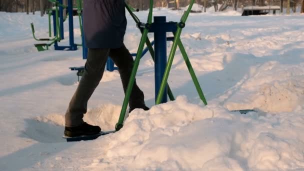 Nahaufnahme der Beine des Mannes macht Übungen auf einem Simulator in einem Winterpark in der Stadt. Seitenansicht. — Stockvideo