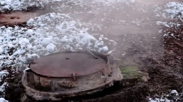 El vapor de cerca proviene de la cubierta sanitaria de las alcantarillas en la nieve. Nieve derretida alrededor . — Vídeos de Stock